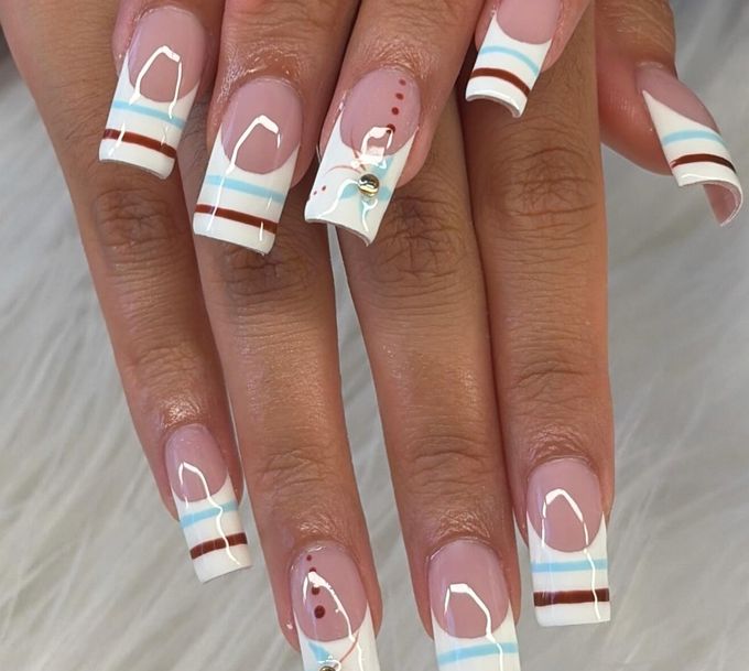 Long square nails with sheer pink bases and white French tips striped in pale blue and dark red, two accent nails with a painted blue flower, tiny red dots and a small rhinestone, over white fur.