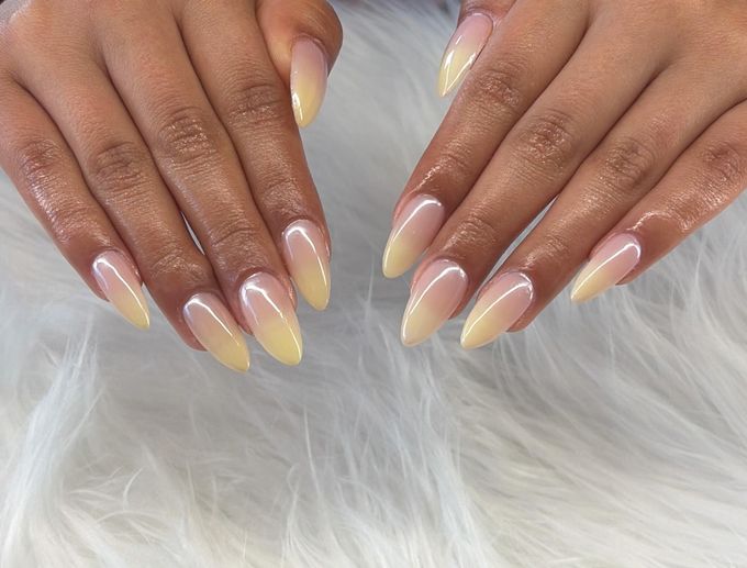 Long almond nails fading from a sheer nude base to soft lemon yellow tips with a pearly shine.