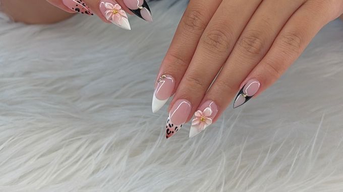 Stiletto nails on a sheer pink base mixing black French tips with a heart cut out, leopard spots over a peach fade, a white French tip and raised peach flowers with gold centres, over white fur.