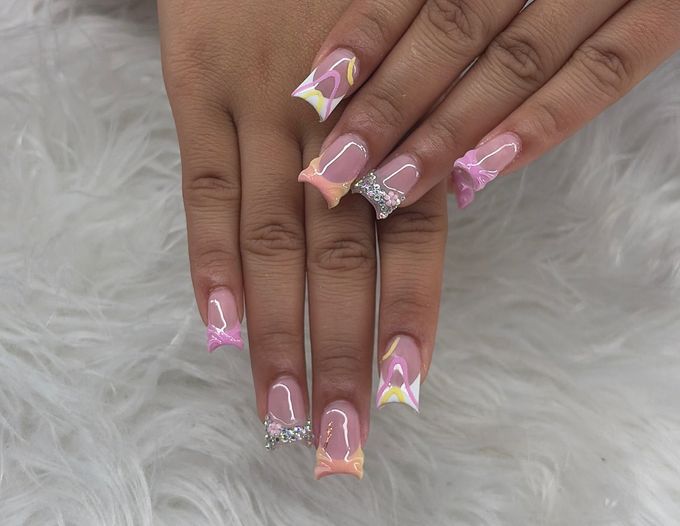 Duck nails with sheer pink bases and mixed tips: peach and pink French tips, white tips with pink and yellow swirl lines, wavy raised pink tips and one tip filled with small crystals, over white fur.