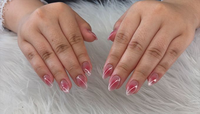 Short almond nails with a raspberry pink aura glow and shimmering tips, hands resting on white fur.