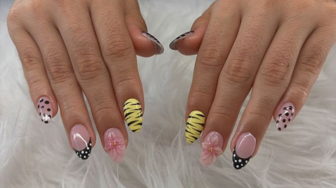 Almond nails mixing yellow tiger stripes, black dots on sheer pink, black French tips with white dots and raised pink flowers with gold centres, hands held over white fur.